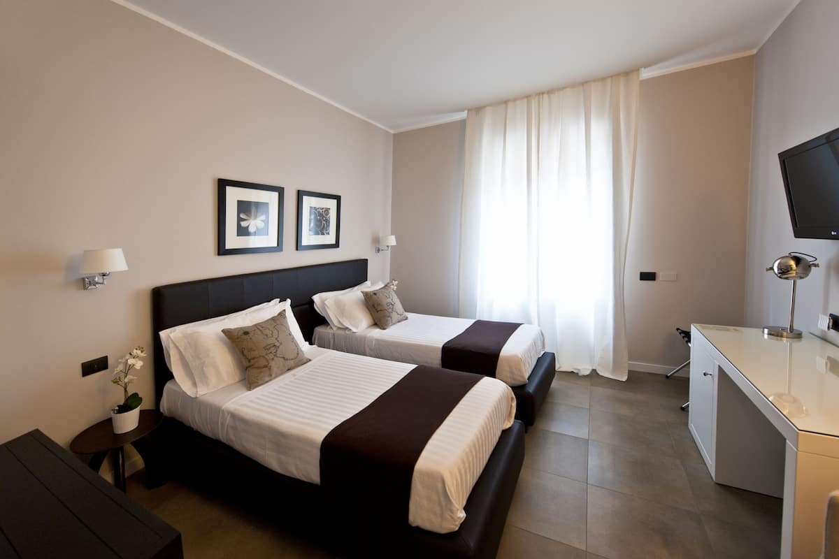 Une chambre d’hôtel avec deux lits, un bureau, une télévision et une fenêtre avec des rideaux.