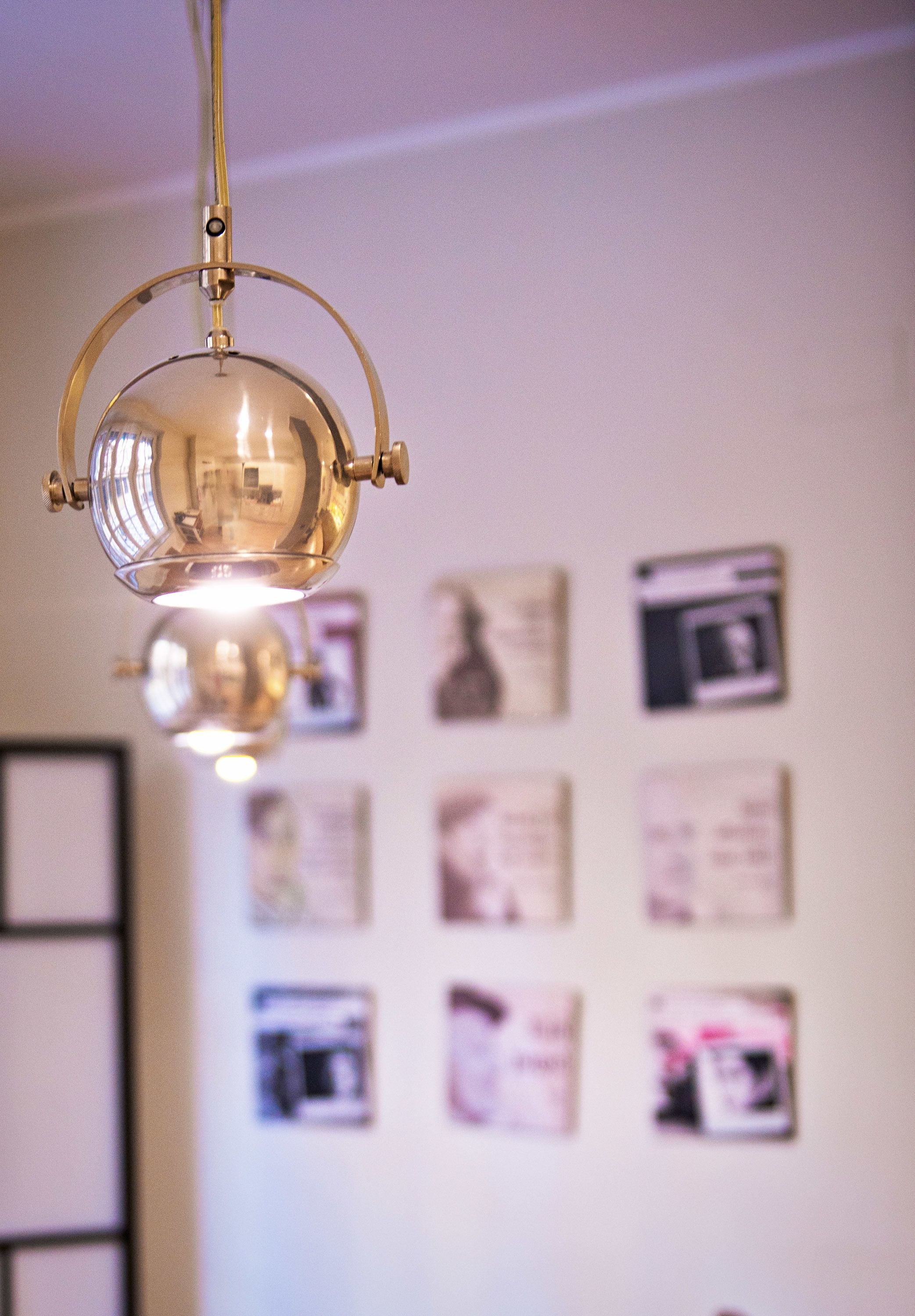 Una lámpara colgante en una habitación con una pared blanca decorada con marcos.