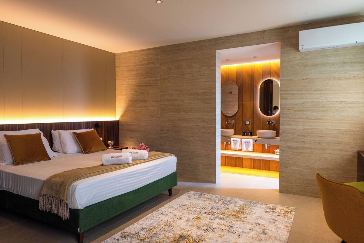 Une chambre d’hôtel moderne avec un grand lit, une salle de bain dotée d’un meuble-lavabo et d’un miroir, et un mur d’accent de couleur verte.