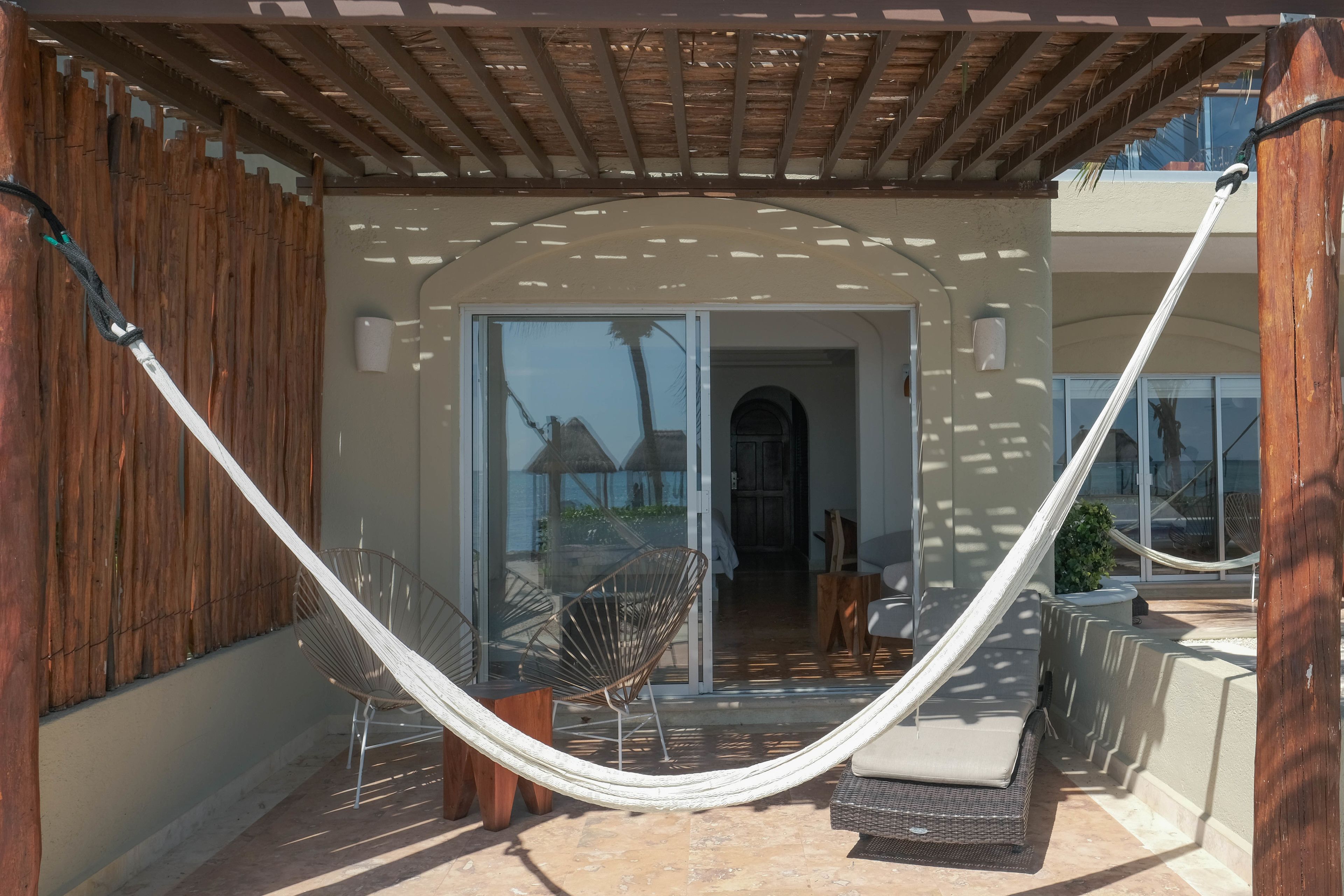 A covered outdoor area with a hammock, wicker furniture, and a view of the interior.