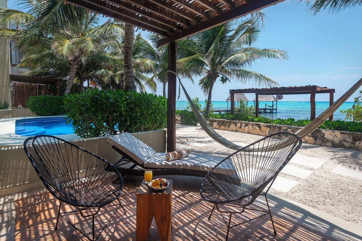 A poolside area with lounge chairs, a wooden table with a fruit bowl, and a view of the ocean.