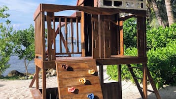 Enjoy a fun day at the beach with a playhouse featuring a slide and climbing holds, surrounded by lush greenery and ocean views.