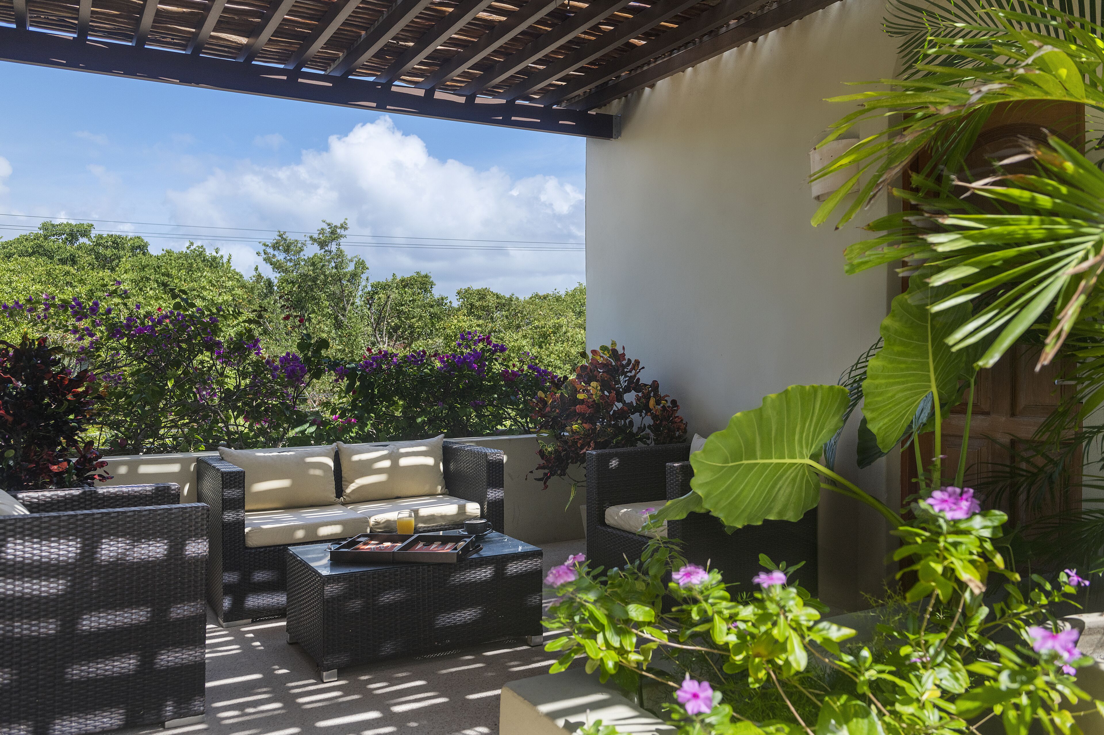 Une terrasse extérieure aménagée avec des meubles en osier, un foyer et une végétation luxuriante.