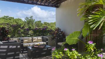 Une terrasse extérieure aménagée avec des meubles en osier, un foyer et une végétation luxuriante.