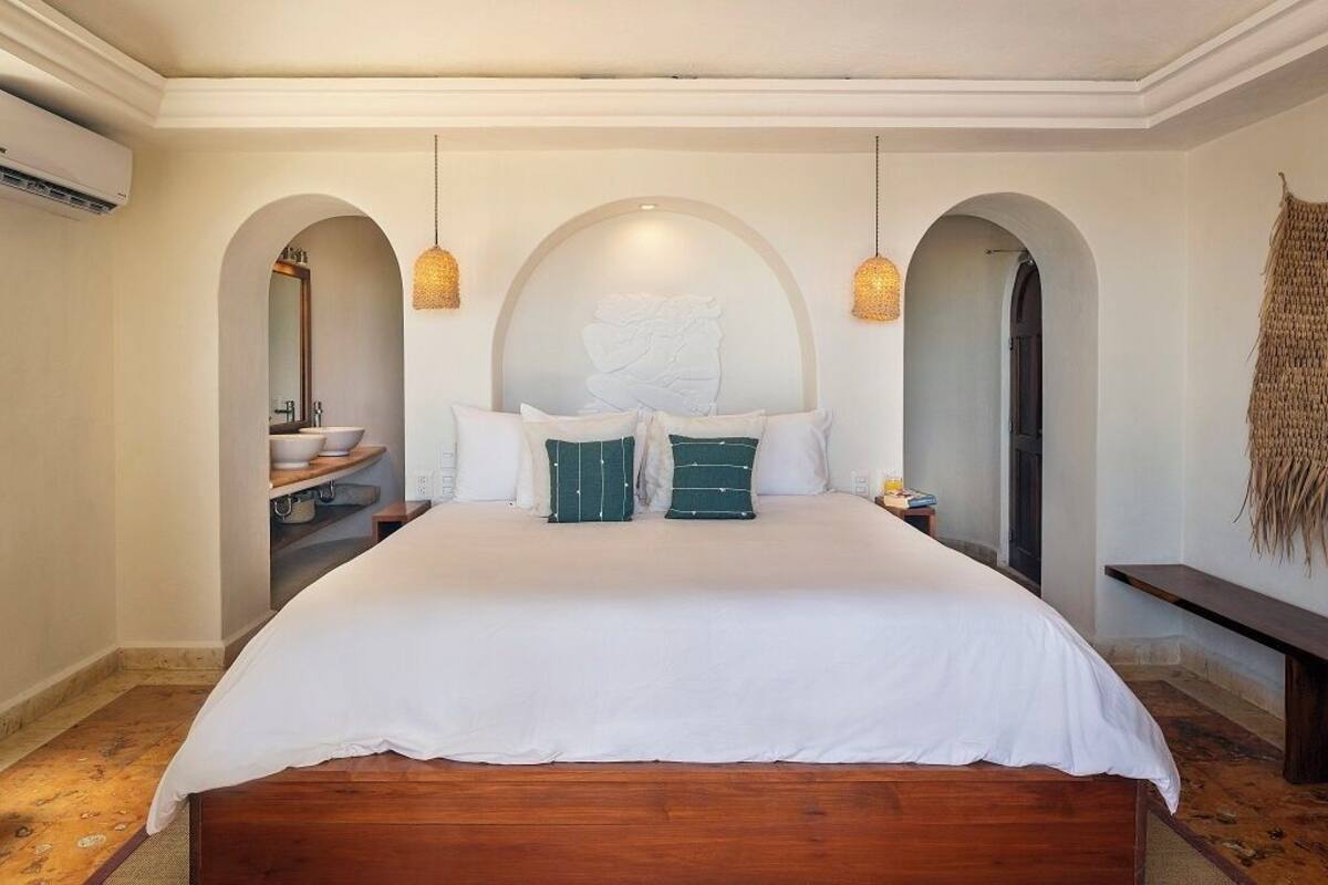 A bedroom with a large bed, two hanging light fixtures, and an arched doorway.