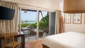 A hotel room with a bed, a TV, a desk with a chair, a balcony with a table and chairs, and framed artwork on the wall. - Mereva Tulum (Tulum)