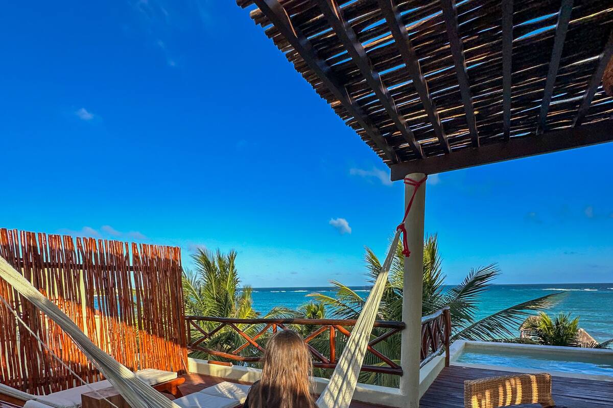 A wooden deck with a hammock, a wooden table, and a view of the ocean.
