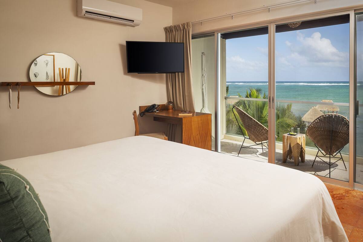 A hotel room with a bed, a desk, a television, and a balcony with chairs and a table.
