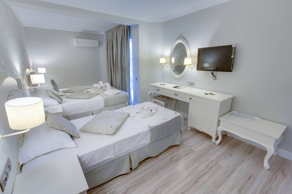 A hotel room with two beds, a desk, a vanity, and a television.
