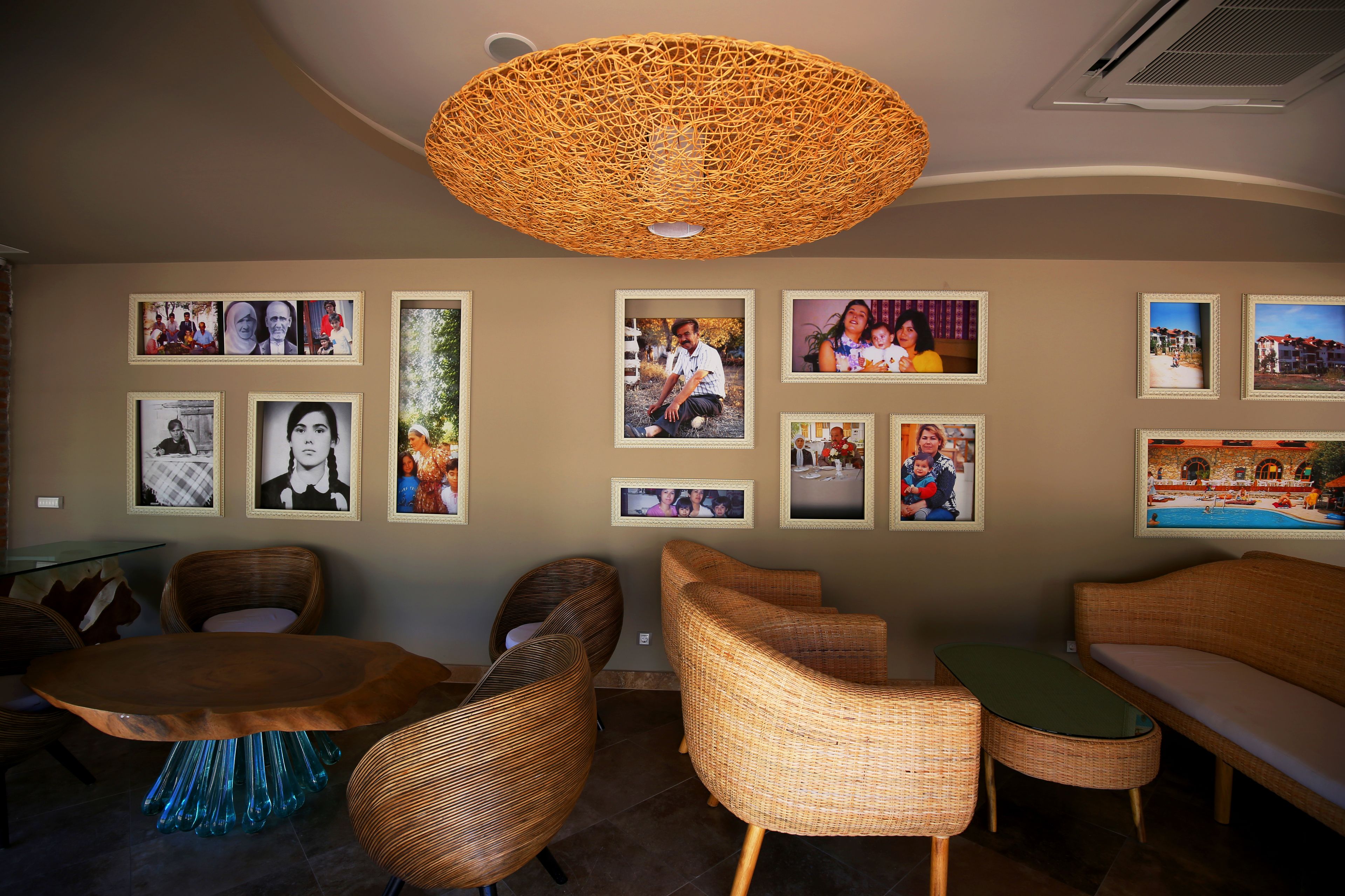 Une pièce meublée de meubles en osier, avec un luminaire suspendu en fibres tressées et des photos encadrées accrochées au mur.