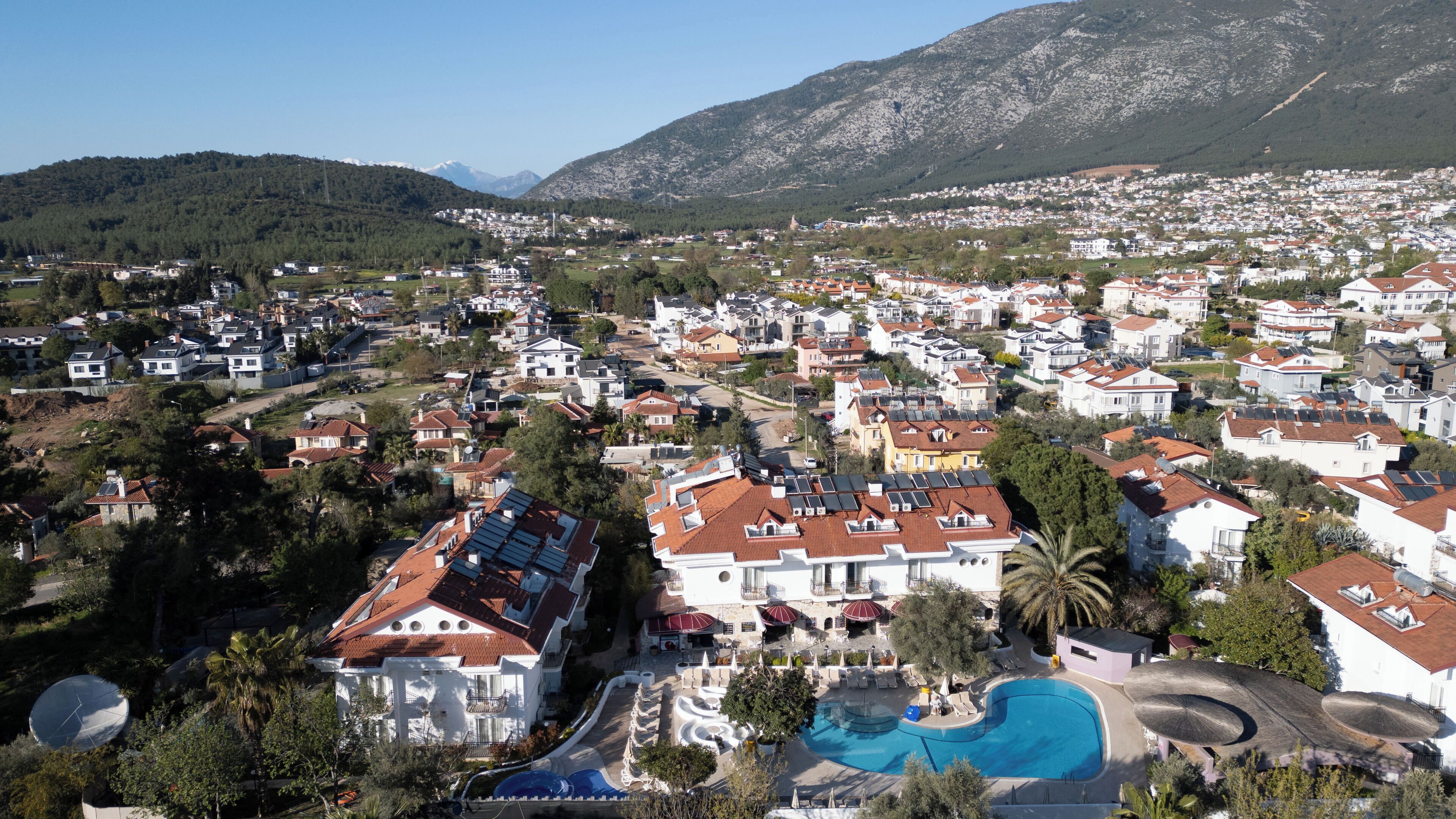 A residential area with a large swimming pool, surrounded by houses with red-tiled roofs and solar panels.