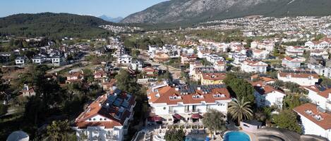 A residential area with a large swimming pool, surrounded by houses with red-tiled roofs and solar panels.