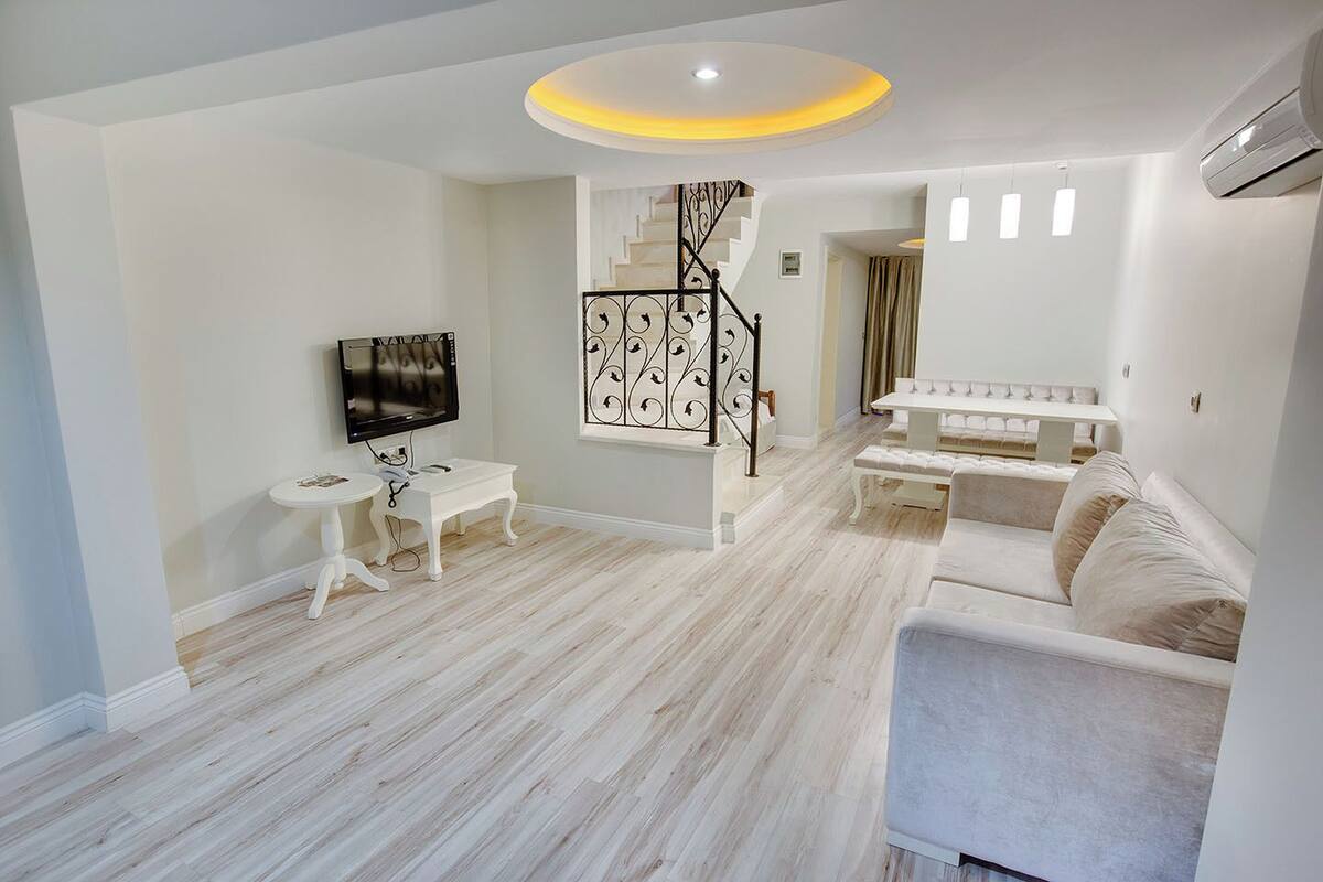 A modern living room with a staircase, a flat-screen TV, a white sofa, and a dining table.