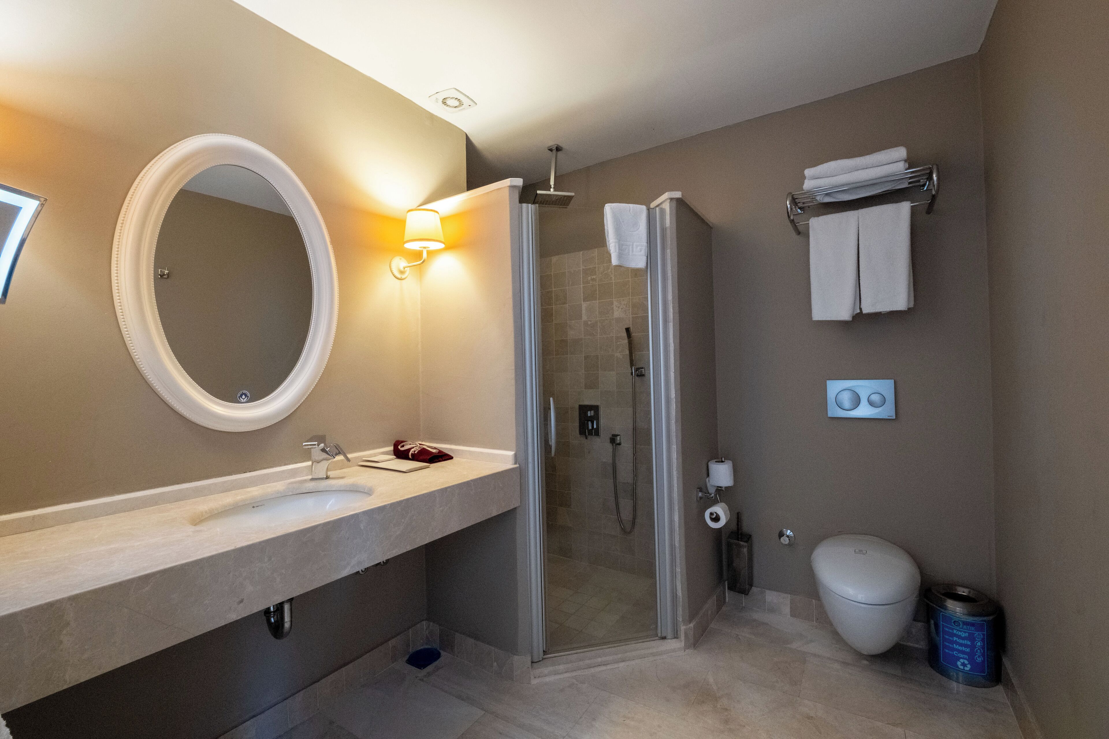 A modern bathroom with a glass-enclosed shower, a round mirror, a sink, and a toilet.