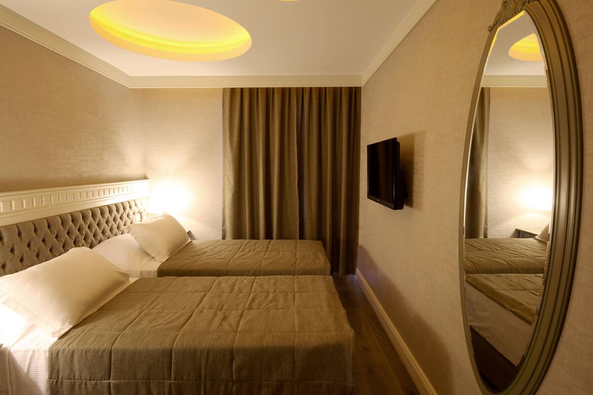 A hotel room with two beds, a large mirror, and a television on the wall.