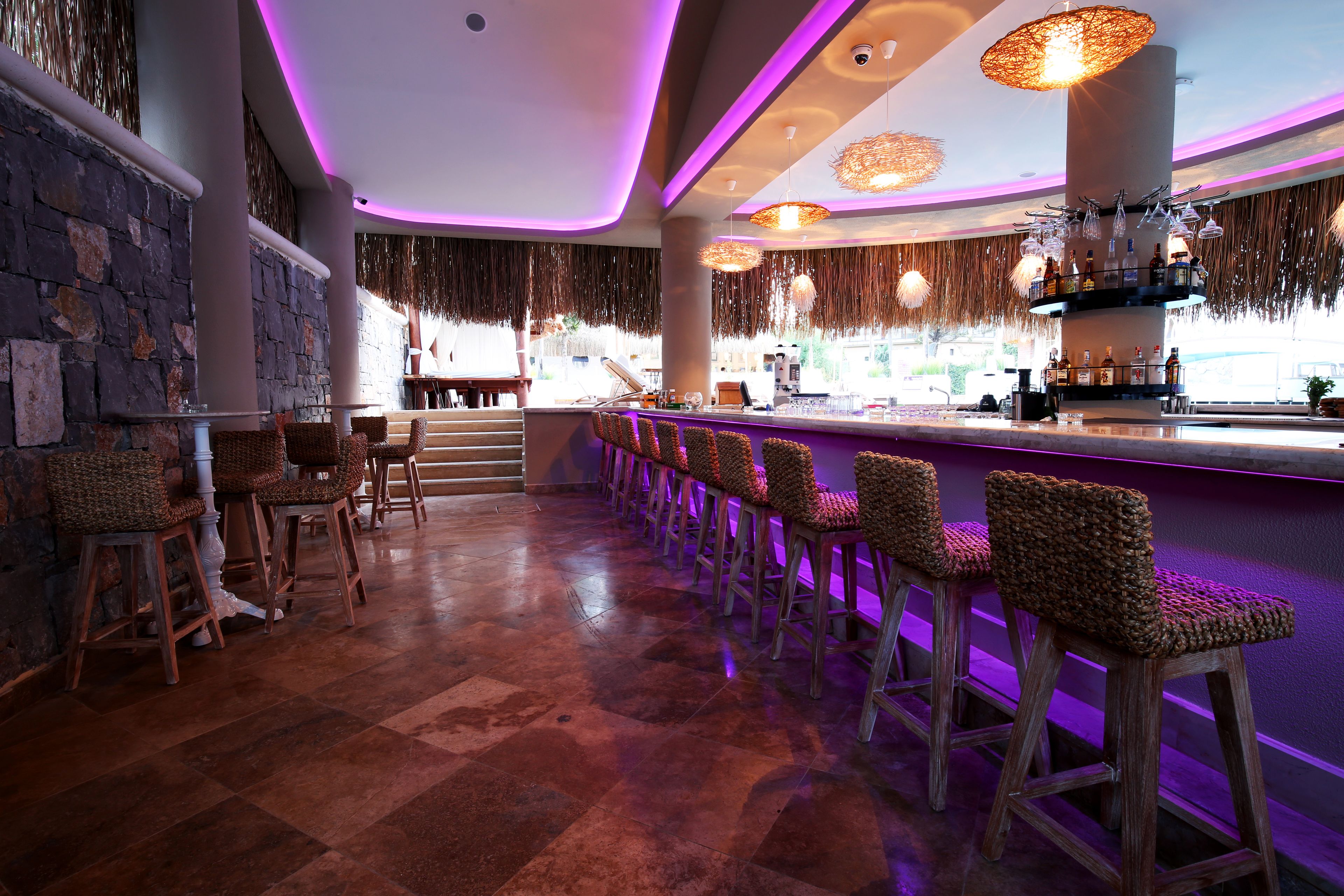 Eine Bar mit einer langen Theke, Weidekorb-Barhocker und hängenden Leuchten.