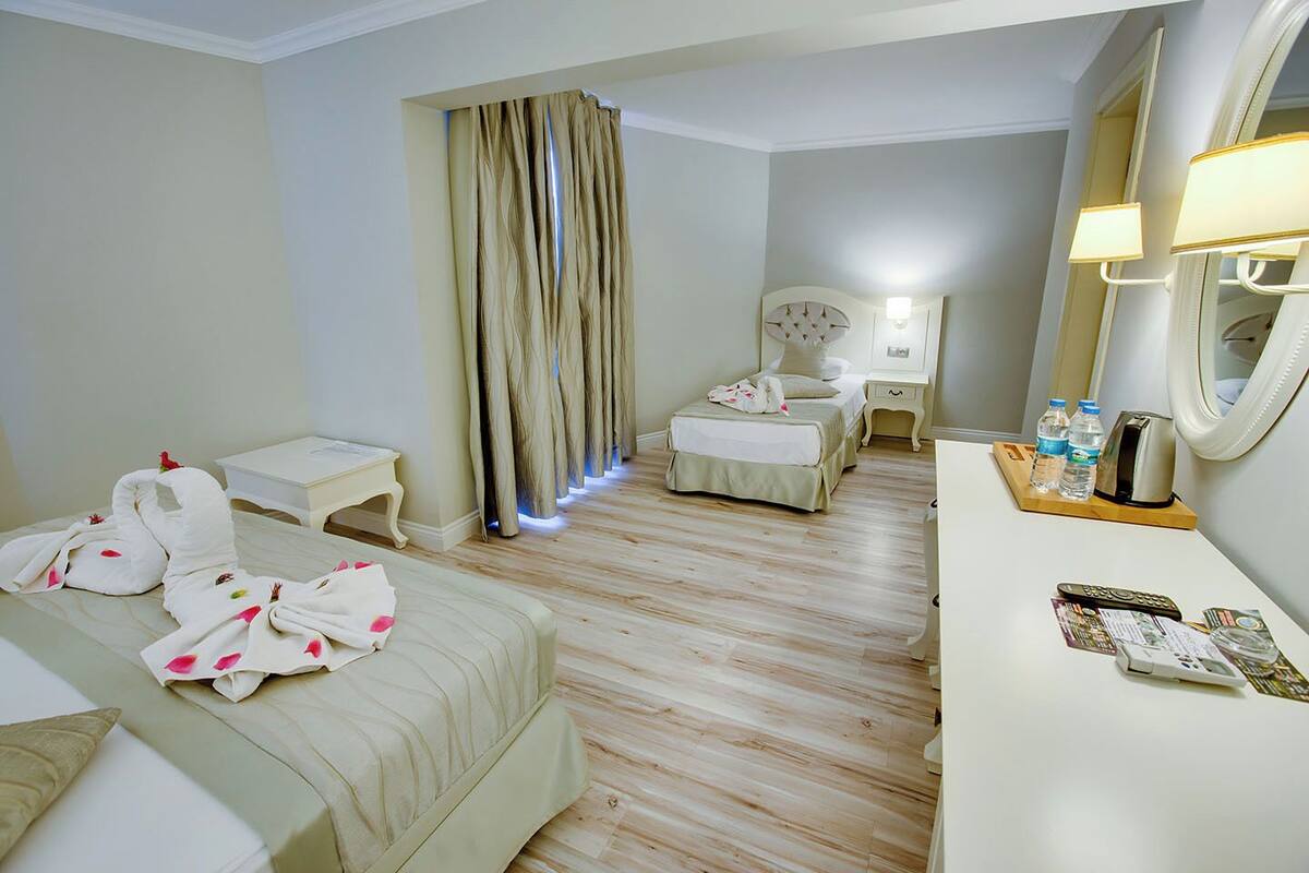 A hotel room with two beds, a bedside table with a lamp, a dresser with toiletries, and a large mirror.