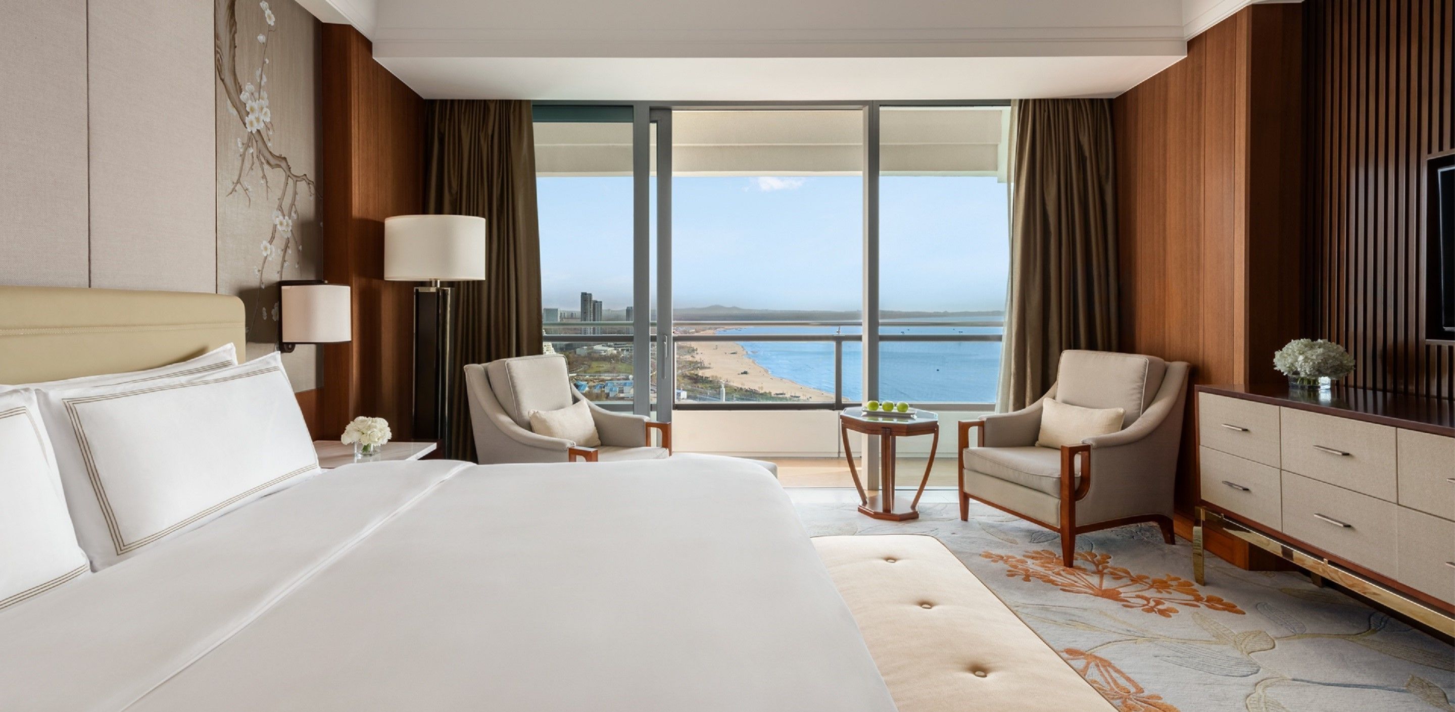 A hotel room with a large bed, two armchairs, a small table, and a view of the sea.