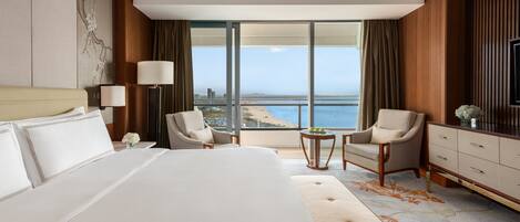 A hotel room with a large bed, two armchairs, a small table, and a view of the sea.