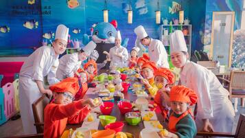 Un grupo de personas con gorros de chef alrededor de una mesa con comida y tazones coloridos, en una habitación con un revestimiento de pared temática de océano azul y repisas con utensilios de cocina.
