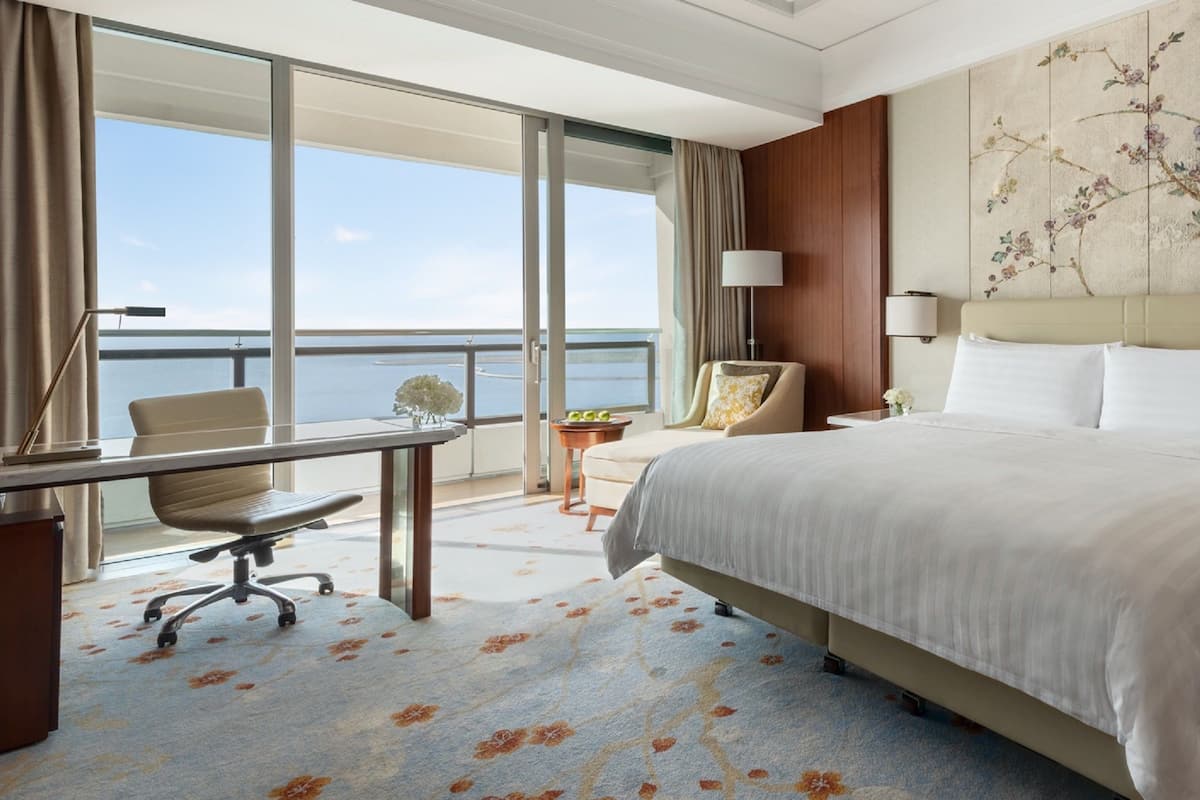 A hotel room with a large bed, a desk, a chair, and a view of the sea.