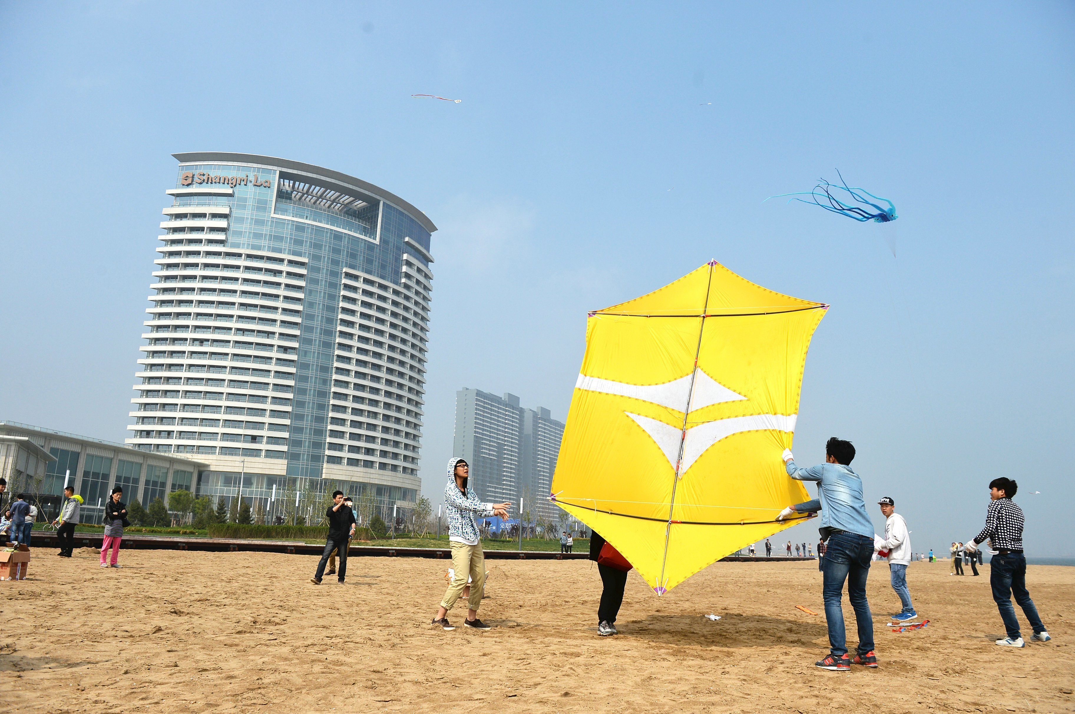 A beach with people flying kites and a tall building in the background.