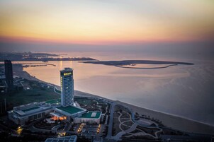 A high-rise hotel with a prominent tower, adjacent to a waterfront with a landscaped area and a parking lot.