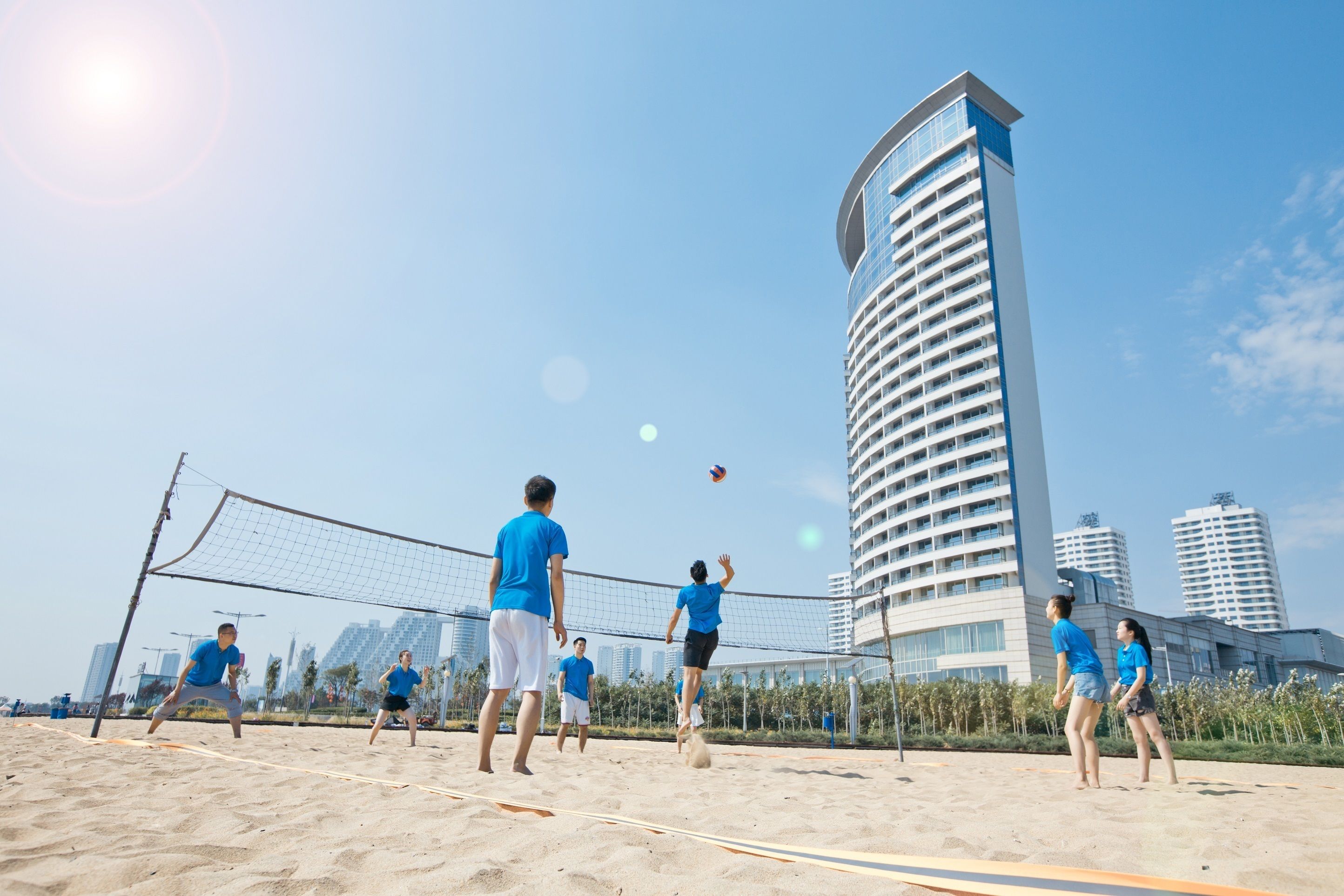 A beach volleyball game on a sandy court with a city skyline in the background.