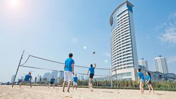 A beach volleyball game on a sandy court with a city skyline in the background.