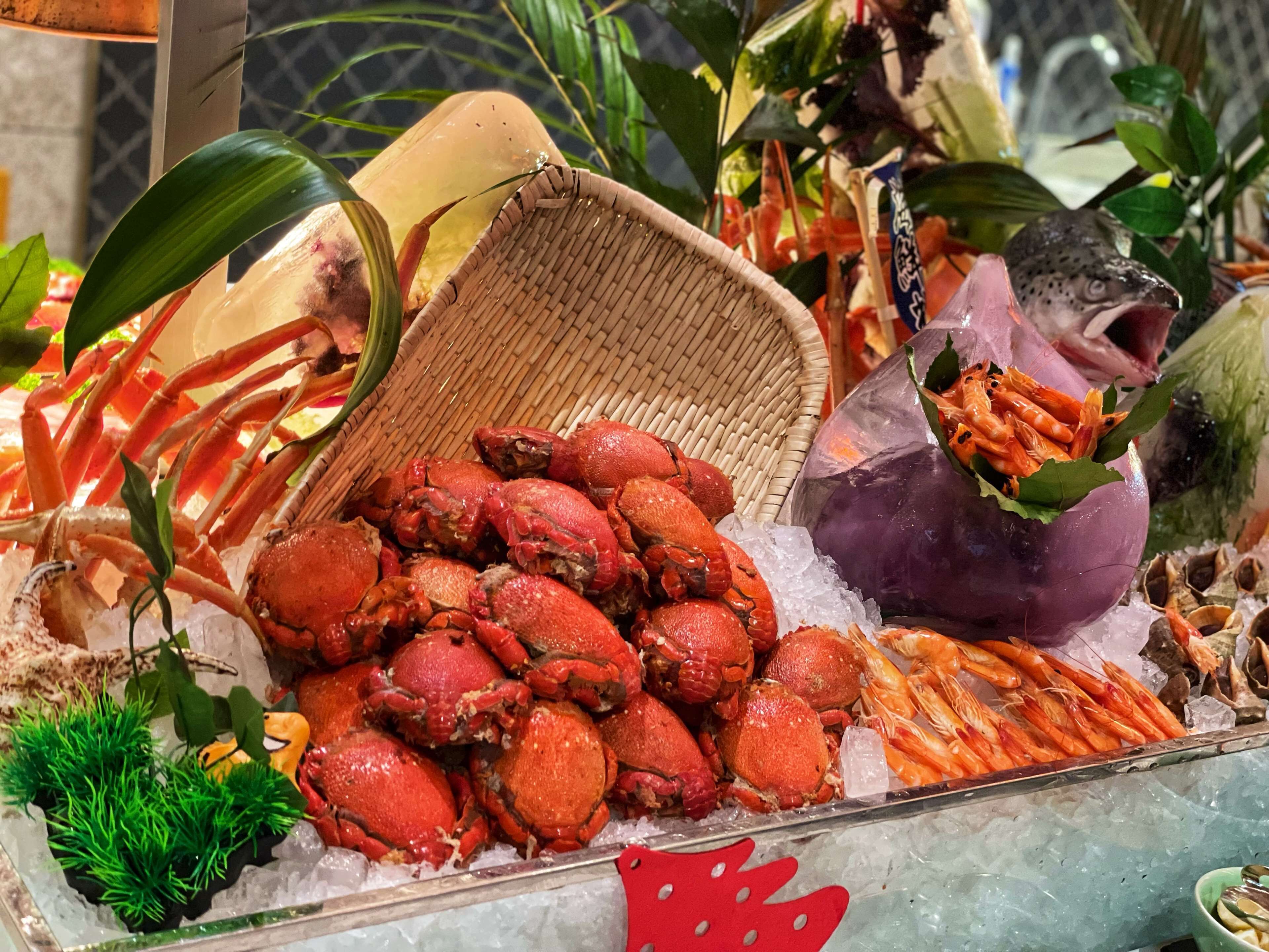 A seafood display with crabs and shrimp on ice, surrounded by decorative elements like leaves and a woven basket.