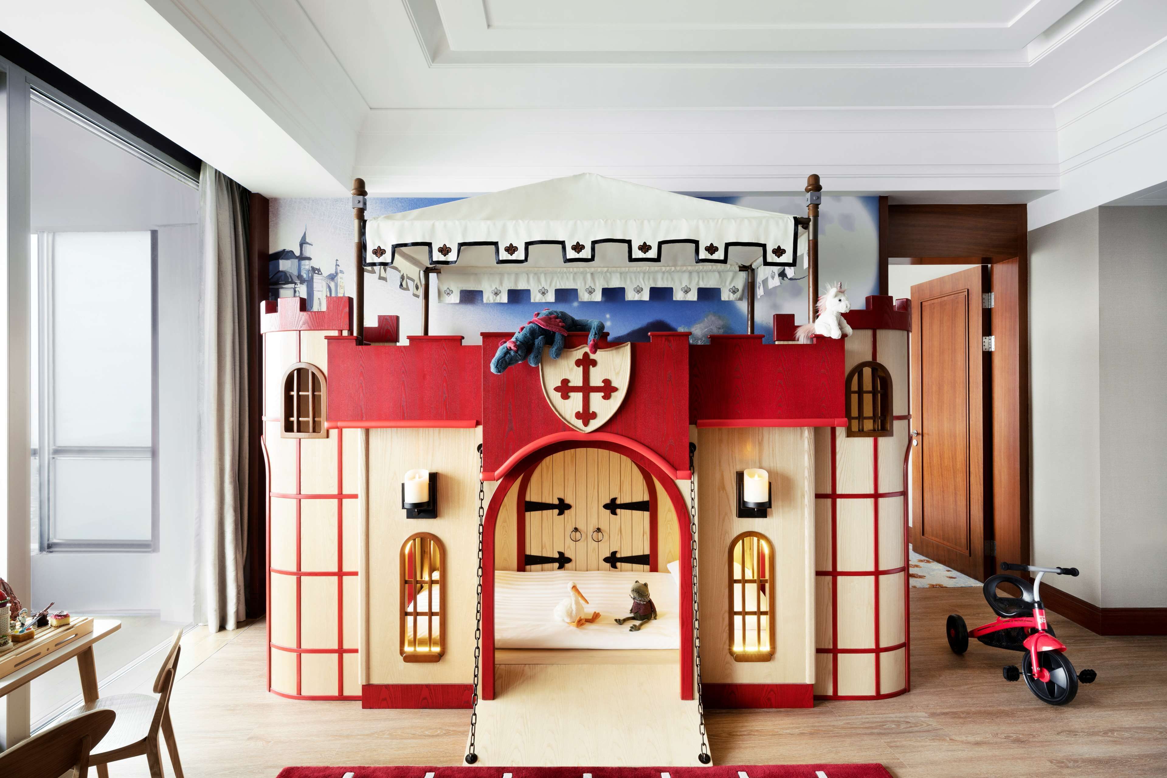Zona de juegos con temática de castillo, incluye una cama, una mesita y un coche de juguete.