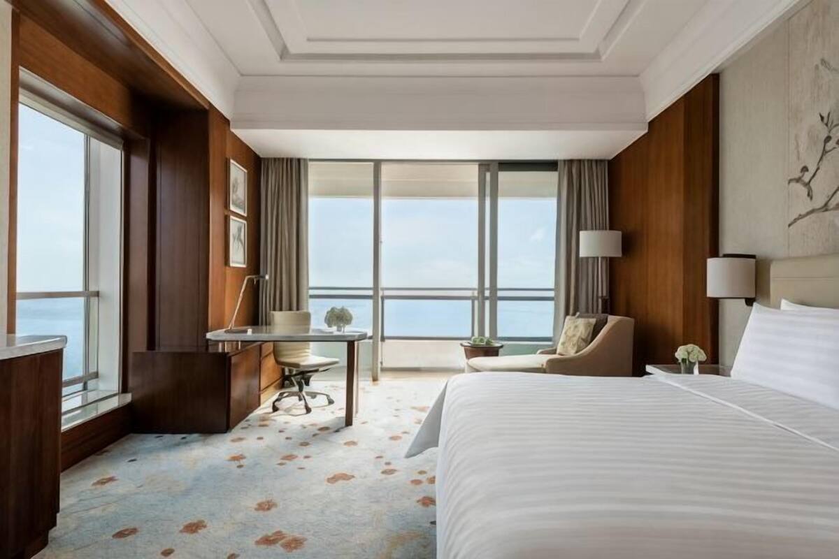 A hotel room with a large bed, a desk, a chair, and a view of the city.