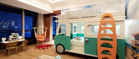 A children's playroom with a toy bus, a hanging chair, and a beach-themed rug.