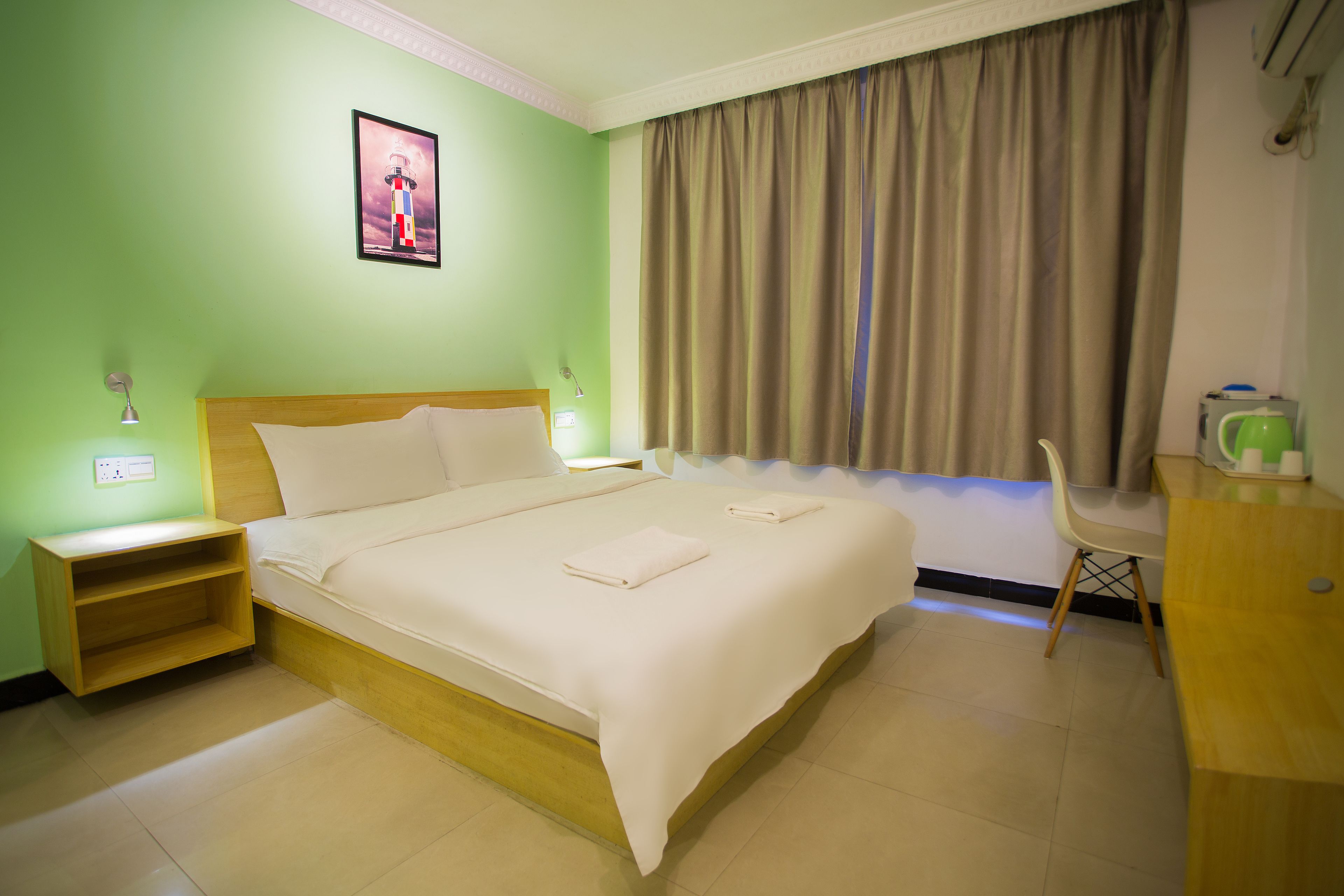 A hotel room with a bed, bedside tables, a desk, a chair, and a curtain.