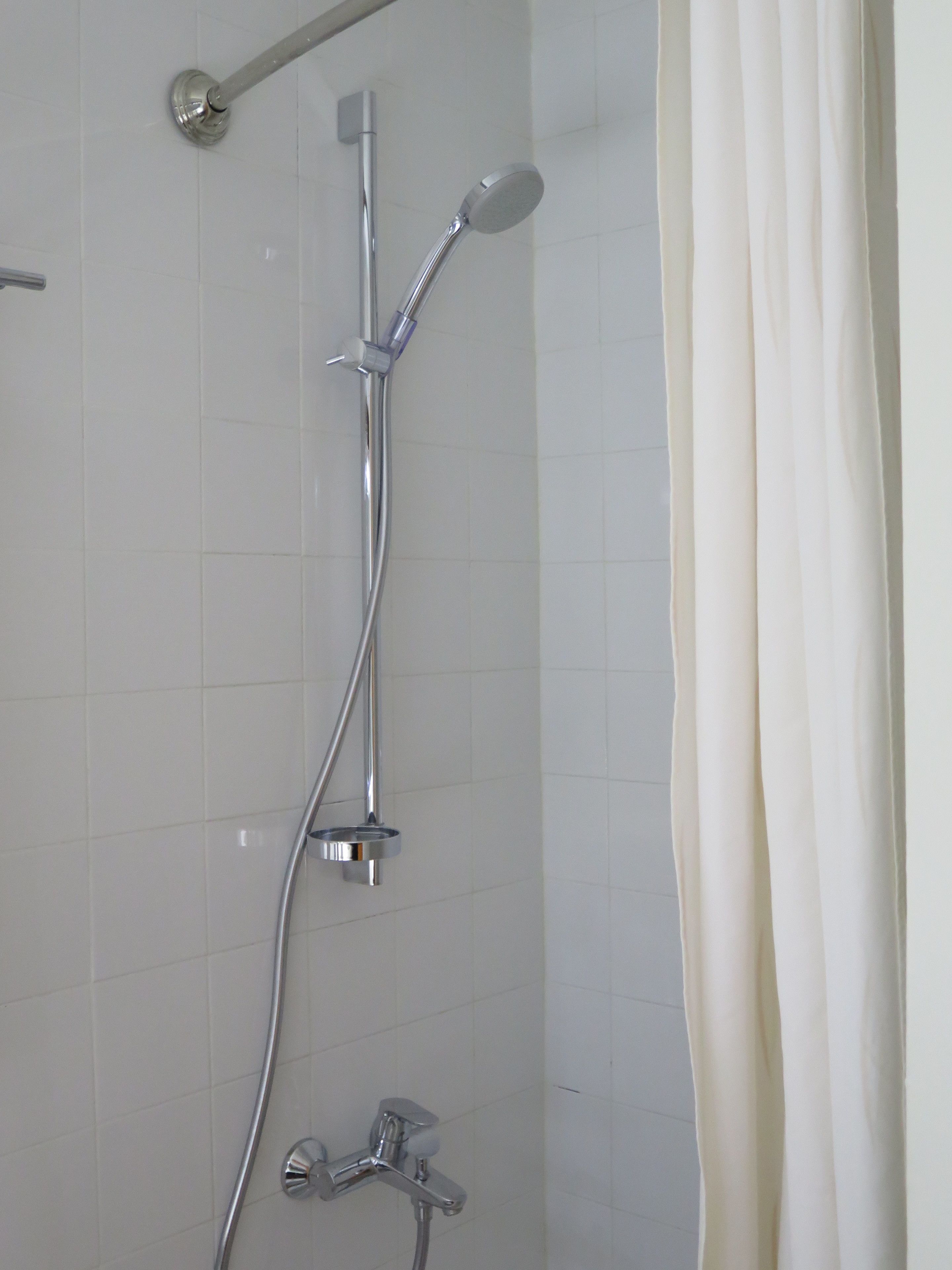 A shower with a handheld showerhead, a wall-mounted faucet, and a handheld showerhead.