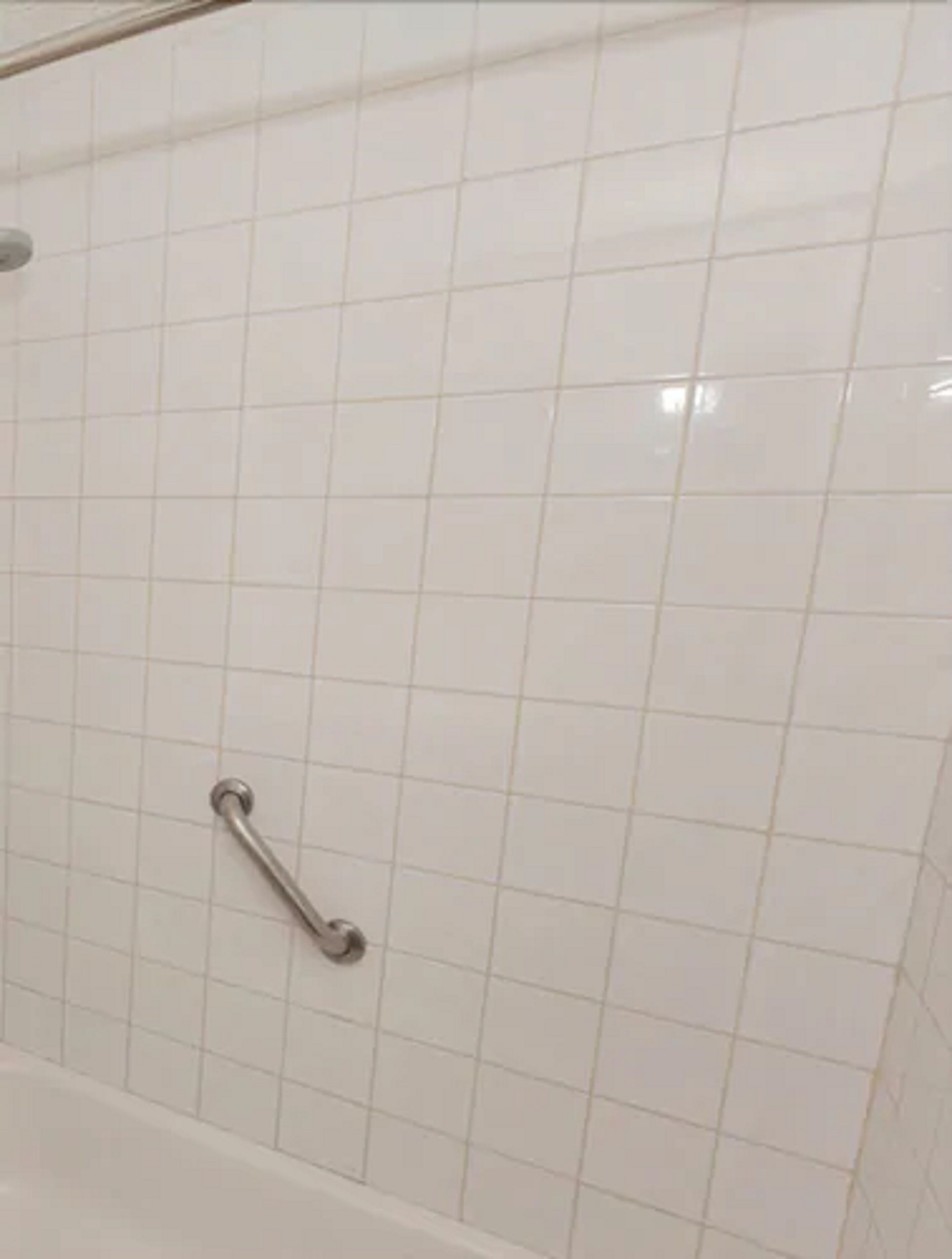 A tiled wall with a metal grab bar.