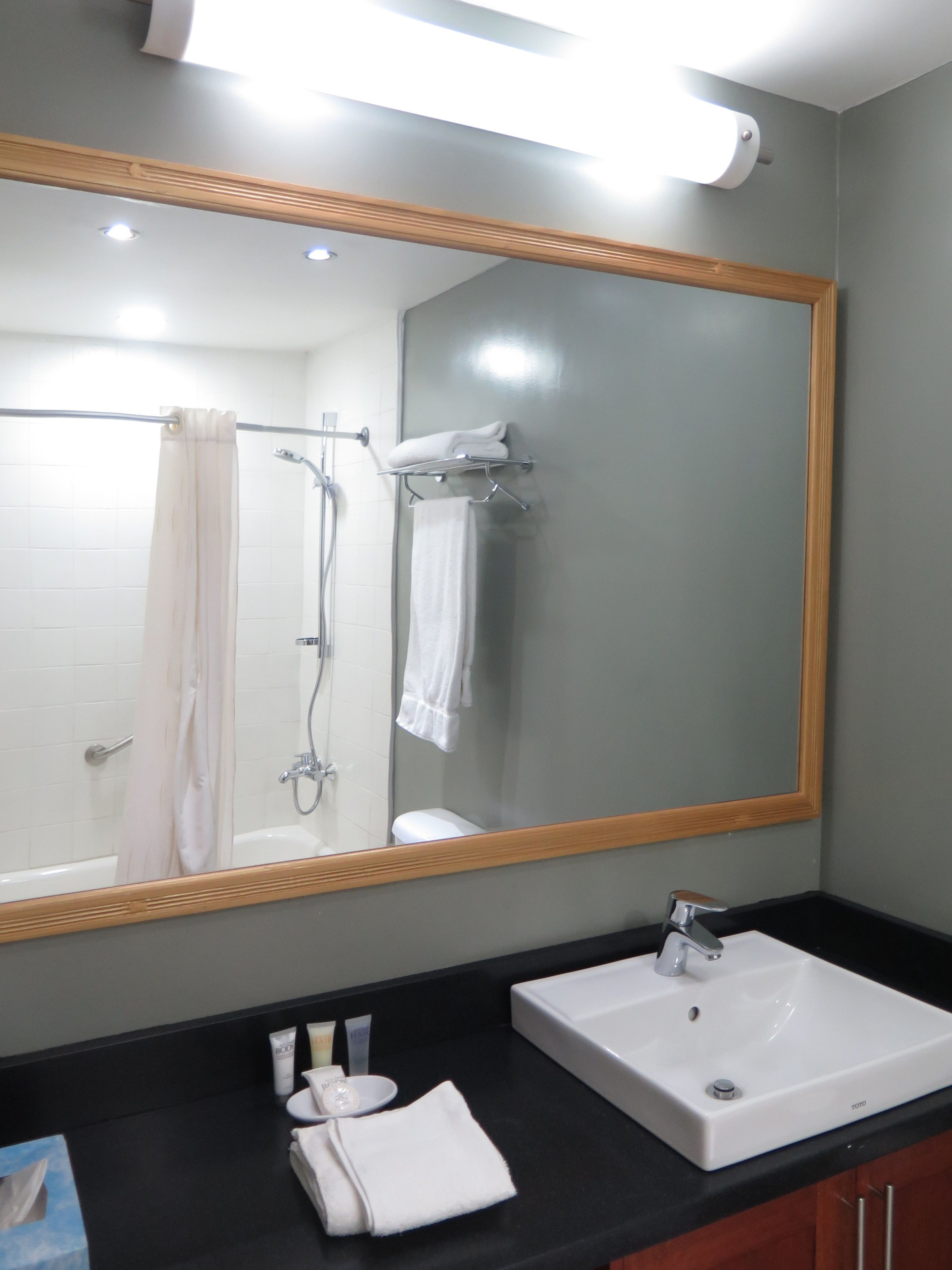 A bathroom with a large mirror, white sink, and shower area.