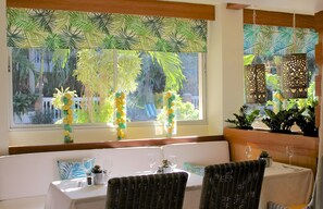 Un coin repas offrant une vue sur la végétation tropicale, une table blanche agrémentée d’un vase de fleurs et des chaises en osier.