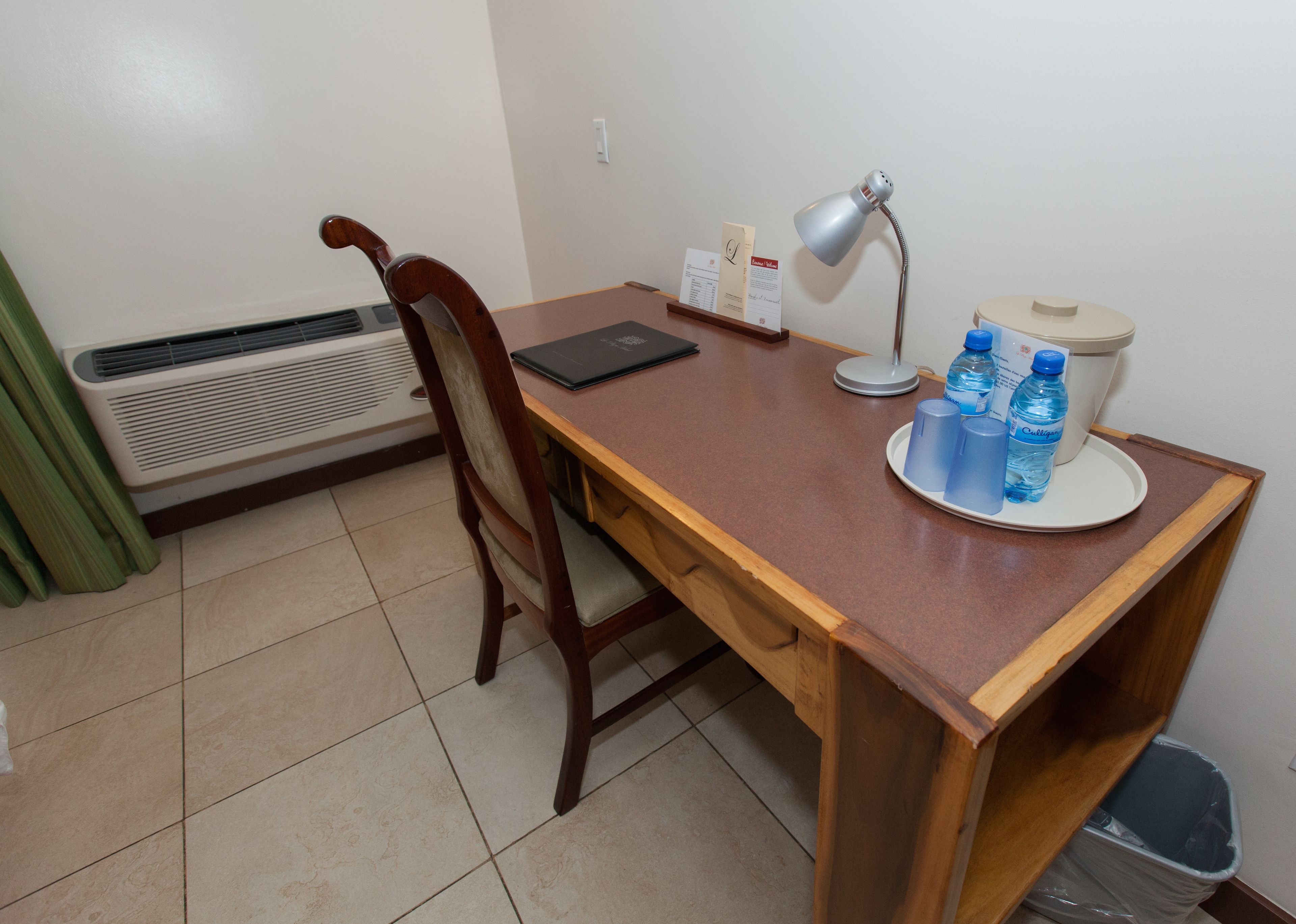 A wooden desk with a laptop, a desk lamp, and water bottles.