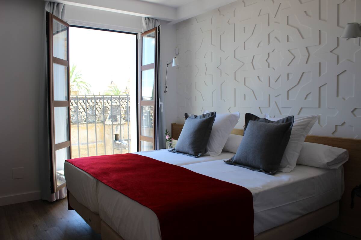 Un dormitorio con una cama, una colcha roja y un papel tapiz estampado.