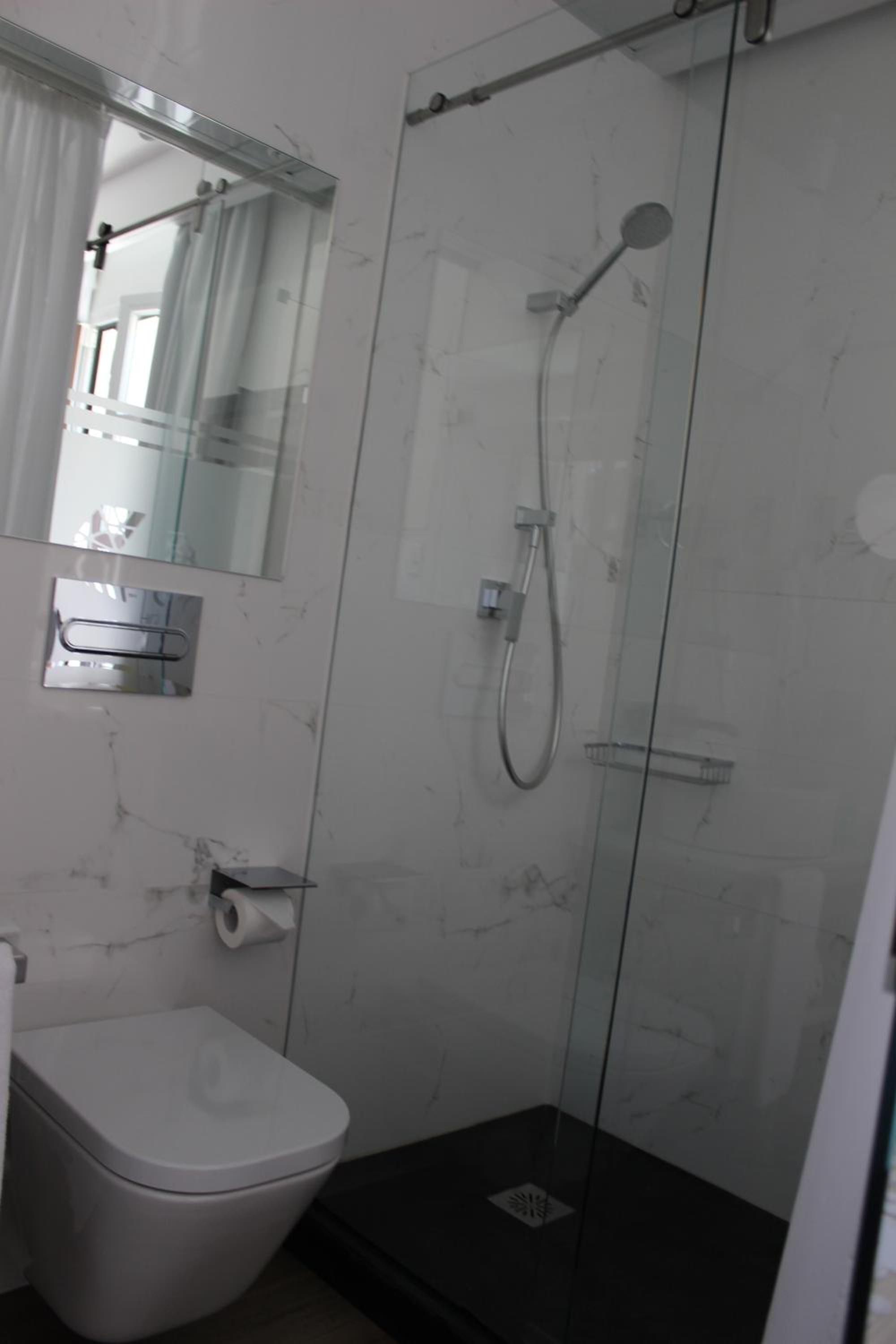 Un baño con cabina de ducha de vidrio, inodoro y espejo.