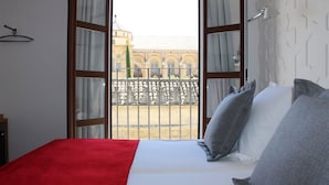 Una habitación de hotel con cama, una colcha roja y vista a un patio con barandilla.