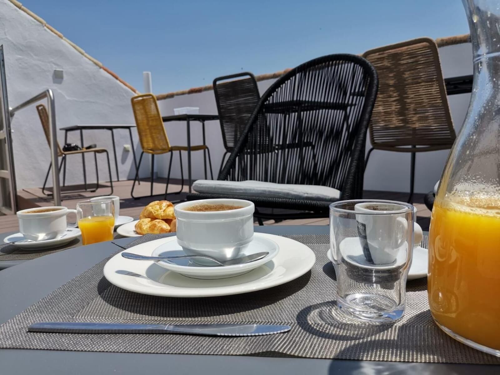 A breakfast setup with coffee, croissants, and orange juice on a table with a view of chairs and a tent in the background.
