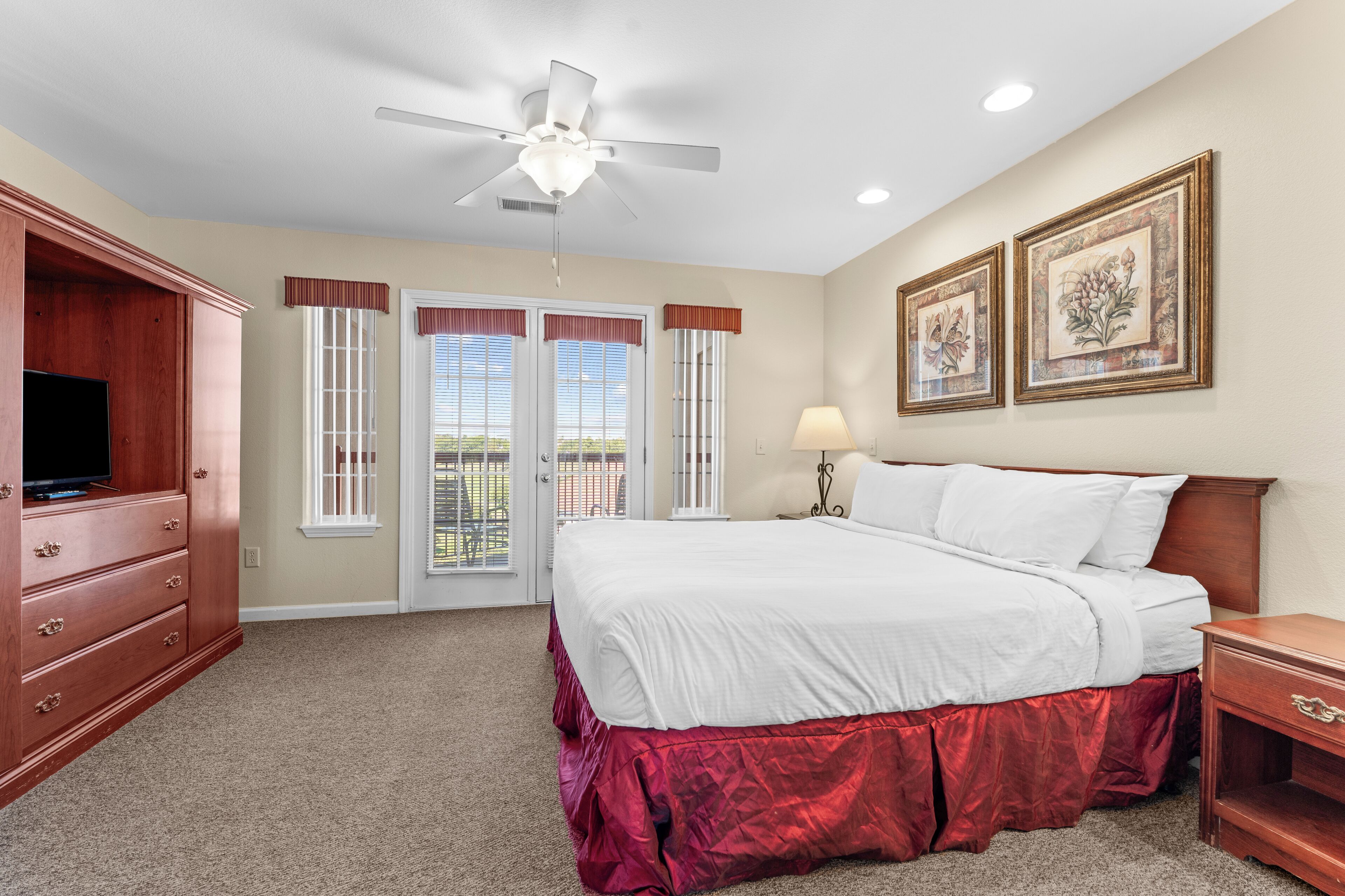 A bedroom with a bed, a ceiling fan, a TV, a dresser, a nightstand, and two framed pictures on the wall.
