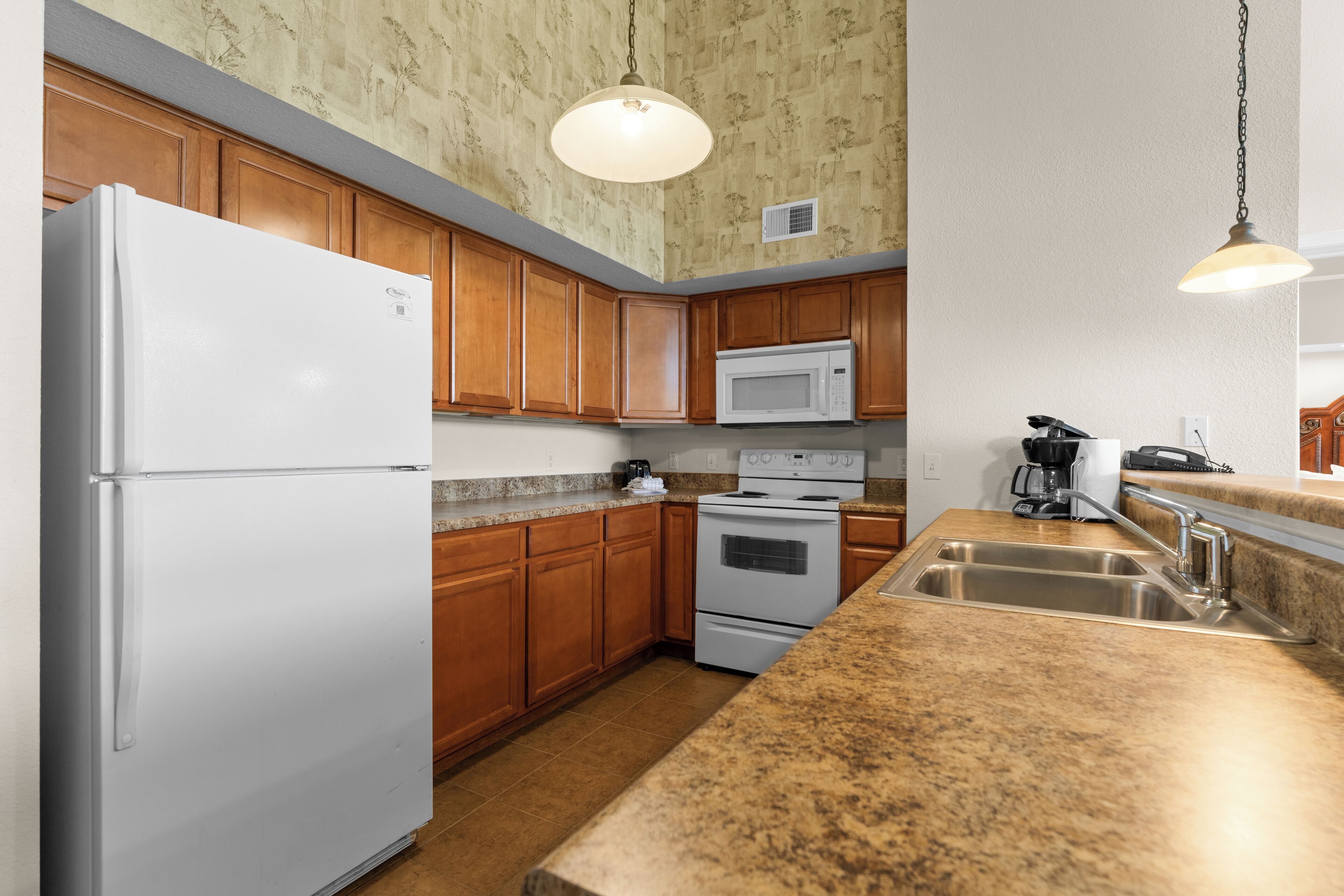 A kitchen with wooden cabinets, a white refrigerator, a microwave, an oven, and a granite countertop.