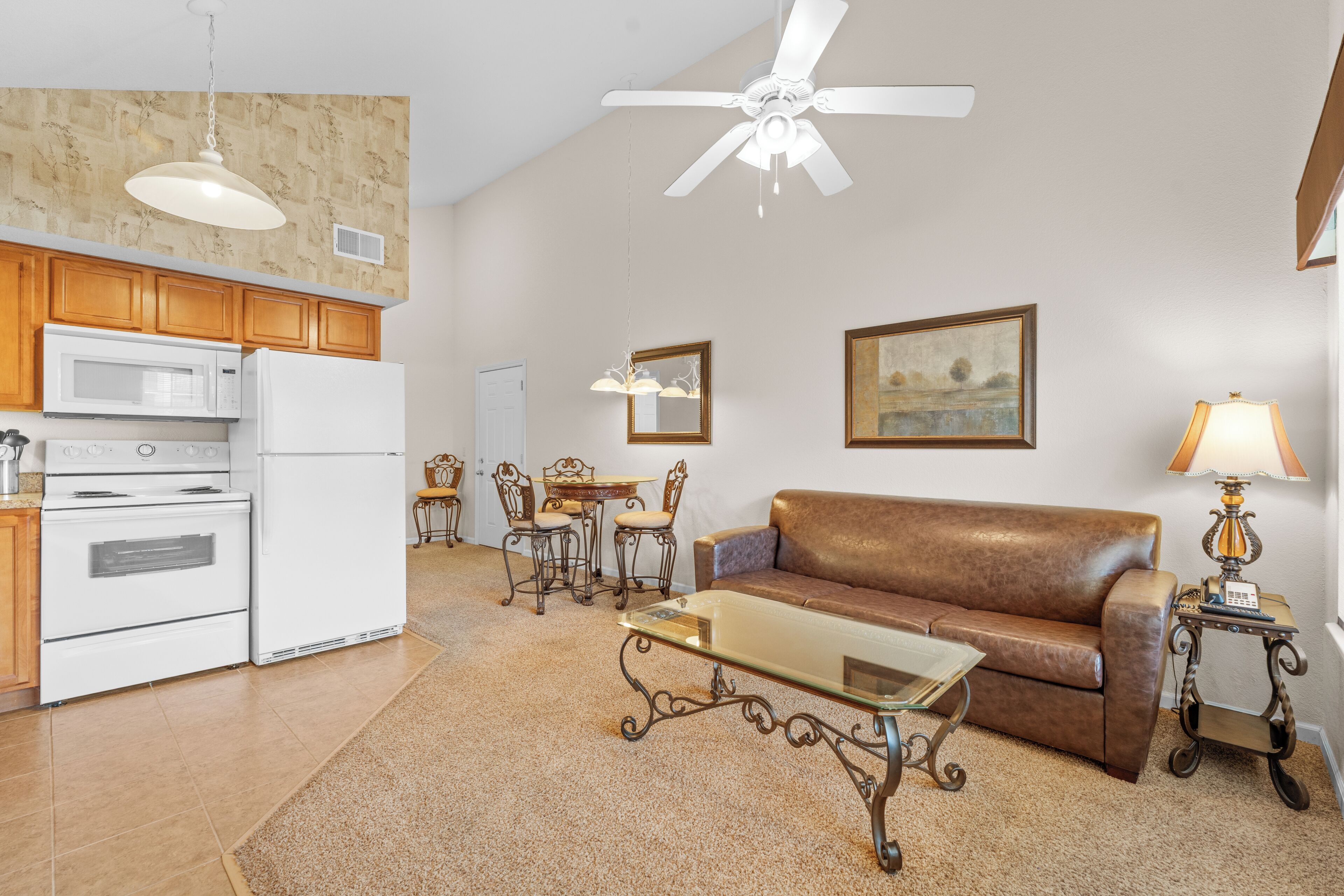 A spacious living area with a brown leather sofa, a glass coffee table, and a dining set. A ceiling fan and pendant lights are visible.