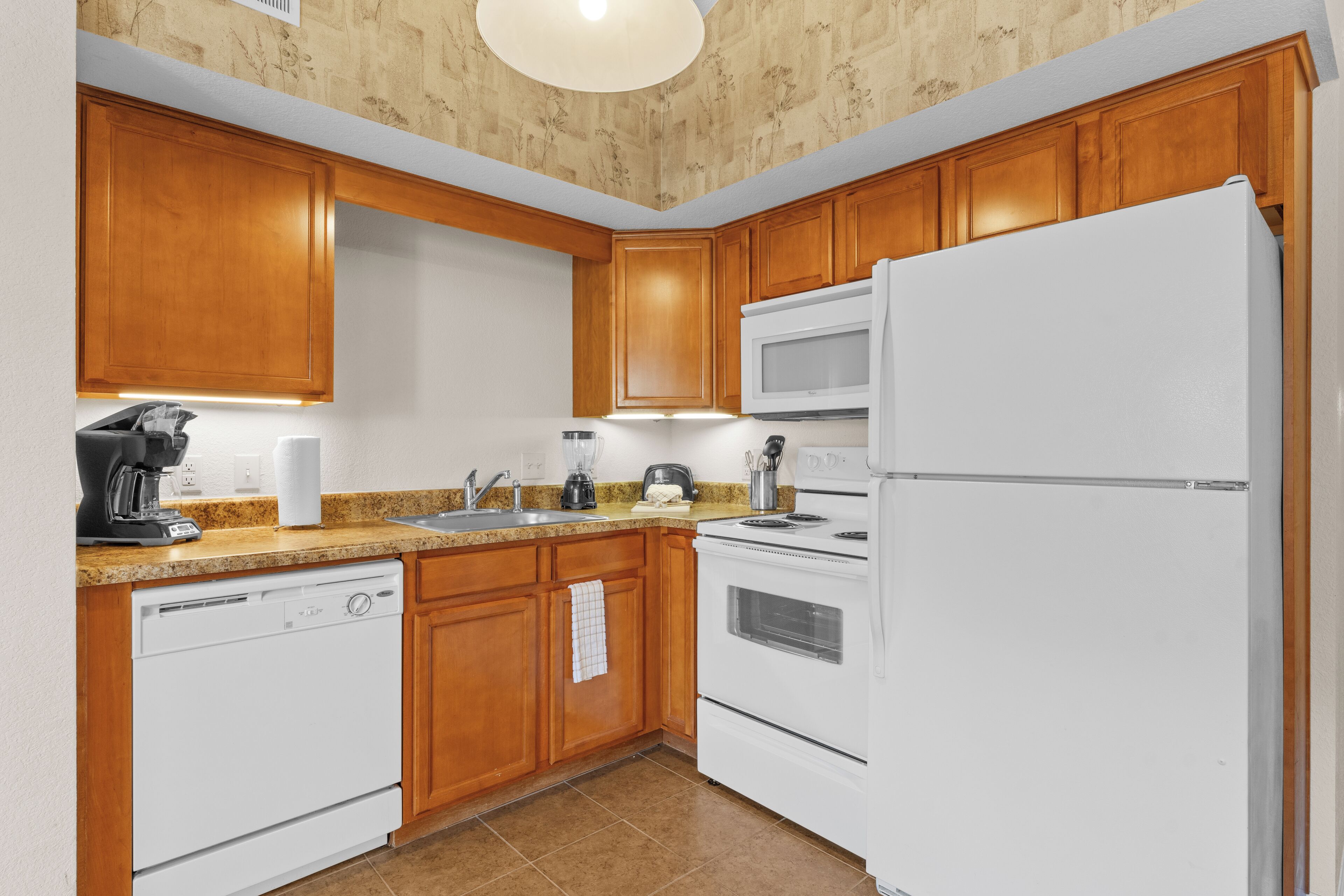 A kitchen with wooden cabinets, a white dishwasher, a white refrigerator, a microwave, and a stove.