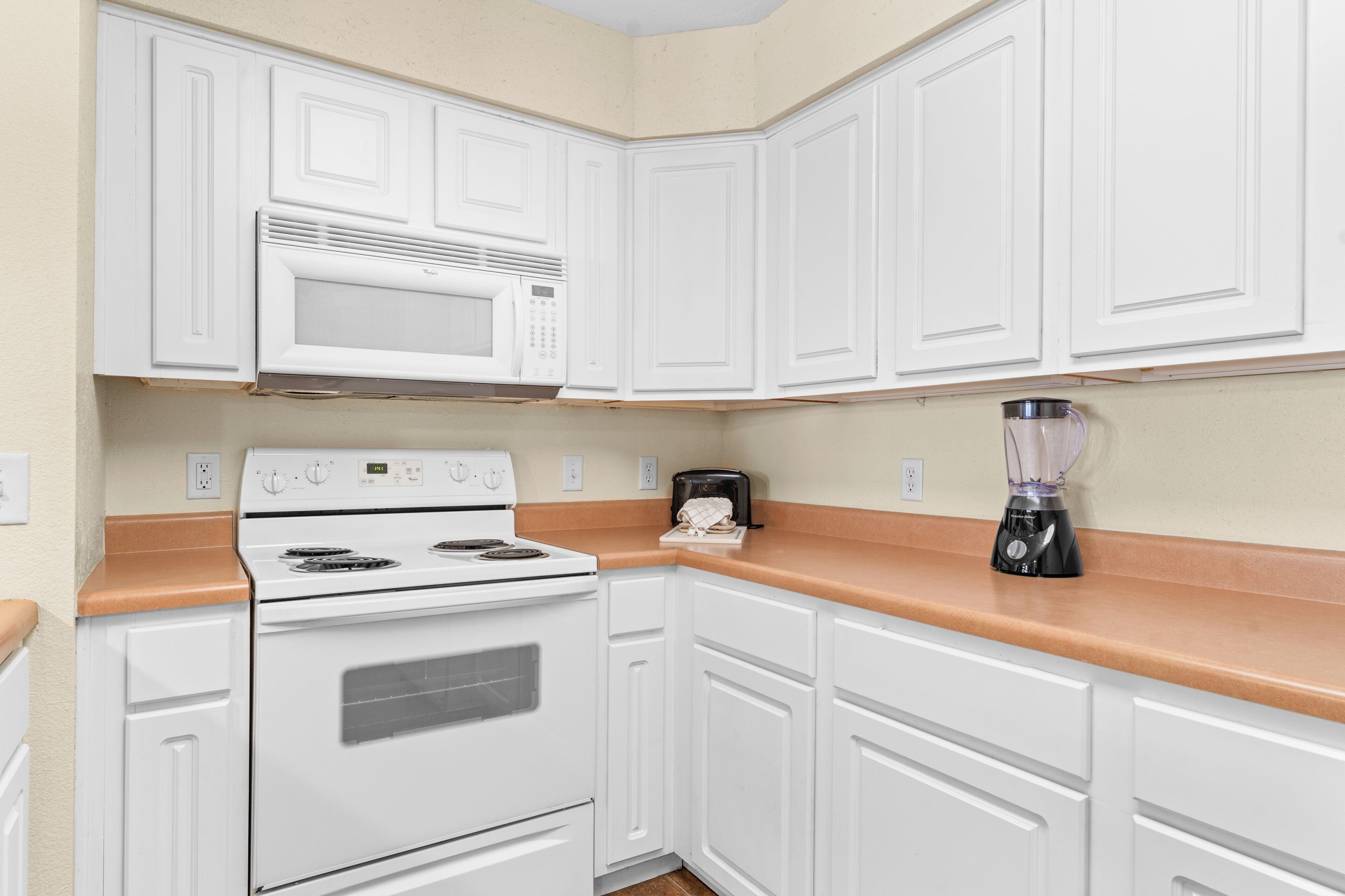 A kitchen with white cabinets, a stove, a microwave, and a blender on the countertop.