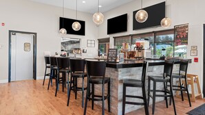Un bar moderno con una isla central, taburetes negros, iluminación colgante y una pizarra con la carta.