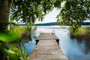A wooden dock extending into a calm lake, surrounded by lush greenery and trees. - Koivulan Kartano (Lohja)